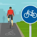 Back view of cyclist cycling on bike path. Bicycle sign and bike